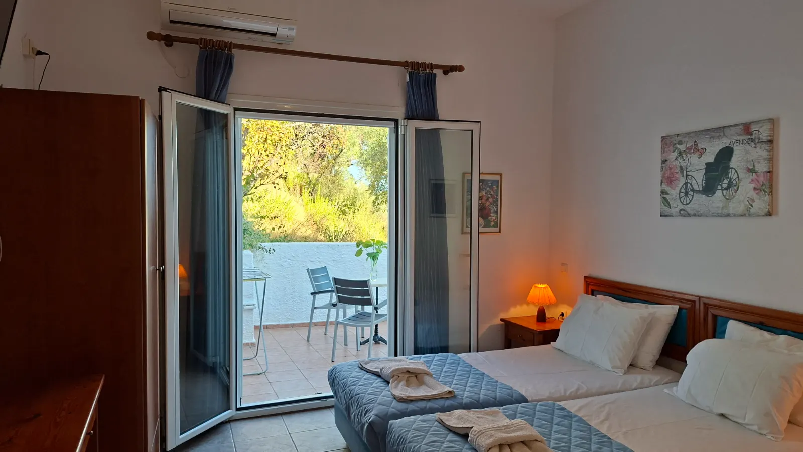 Interior view of the Studio with Balcony twin beds, showing the open balcony doors that lead directly to the outdoor seating area.