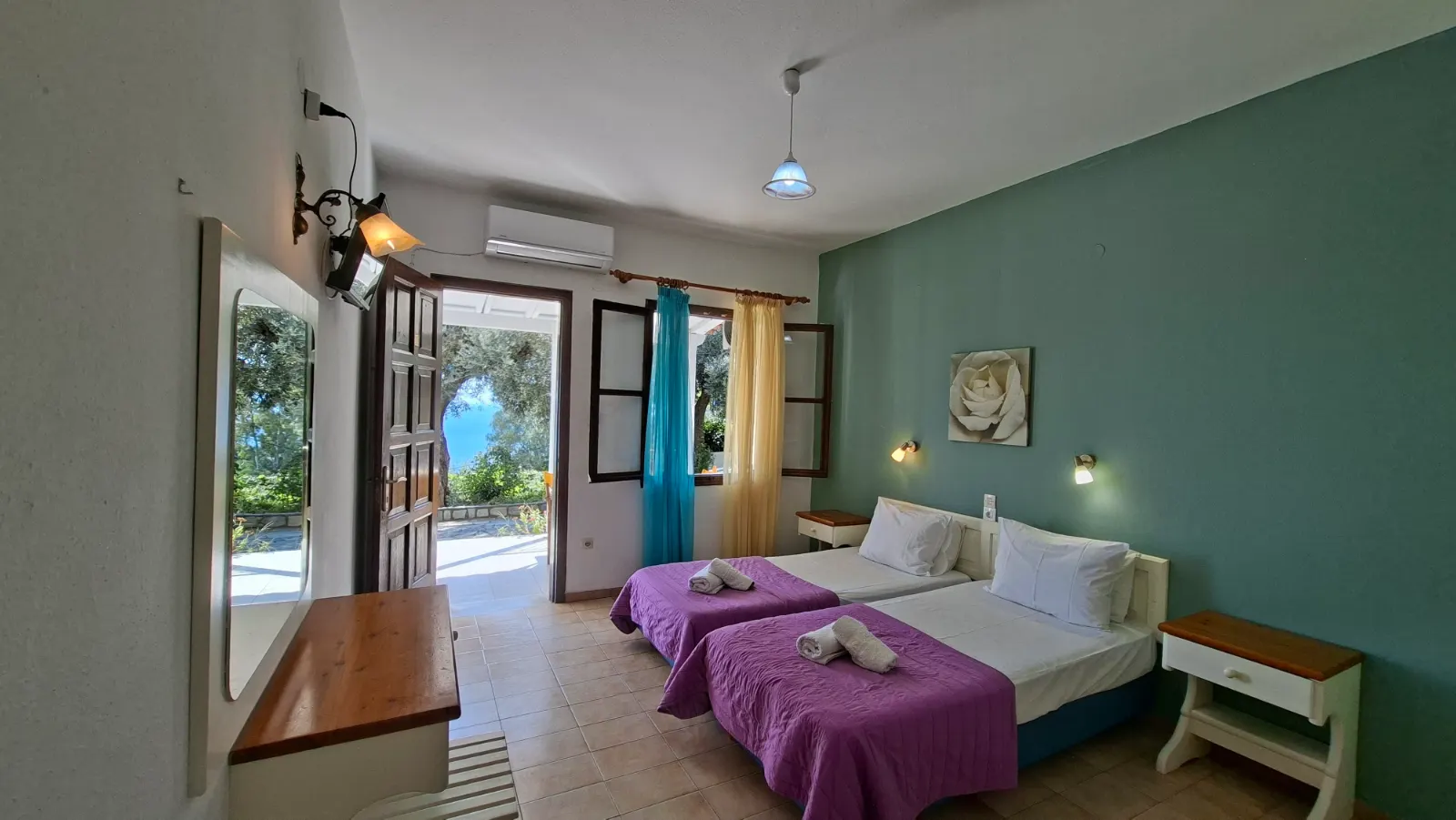 View of the Studio with Terrace featuring twin beds, and a window and door providing a lush greenery view. Studios in Agia Paraskevi Skiathos.
